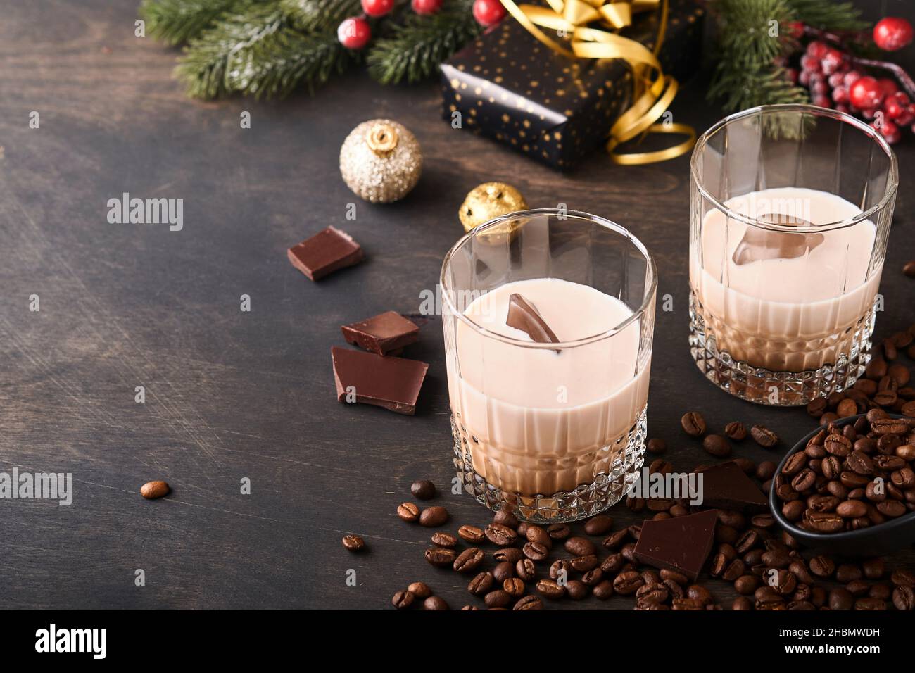 Bicchiere di crema irlandese liquore baileys con ghiaccio, caffè torrefatto in chicchi, cannella, decorazioni natalizie e cioccolato su tavola di fondo in legno scuro. Chris Foto Stock