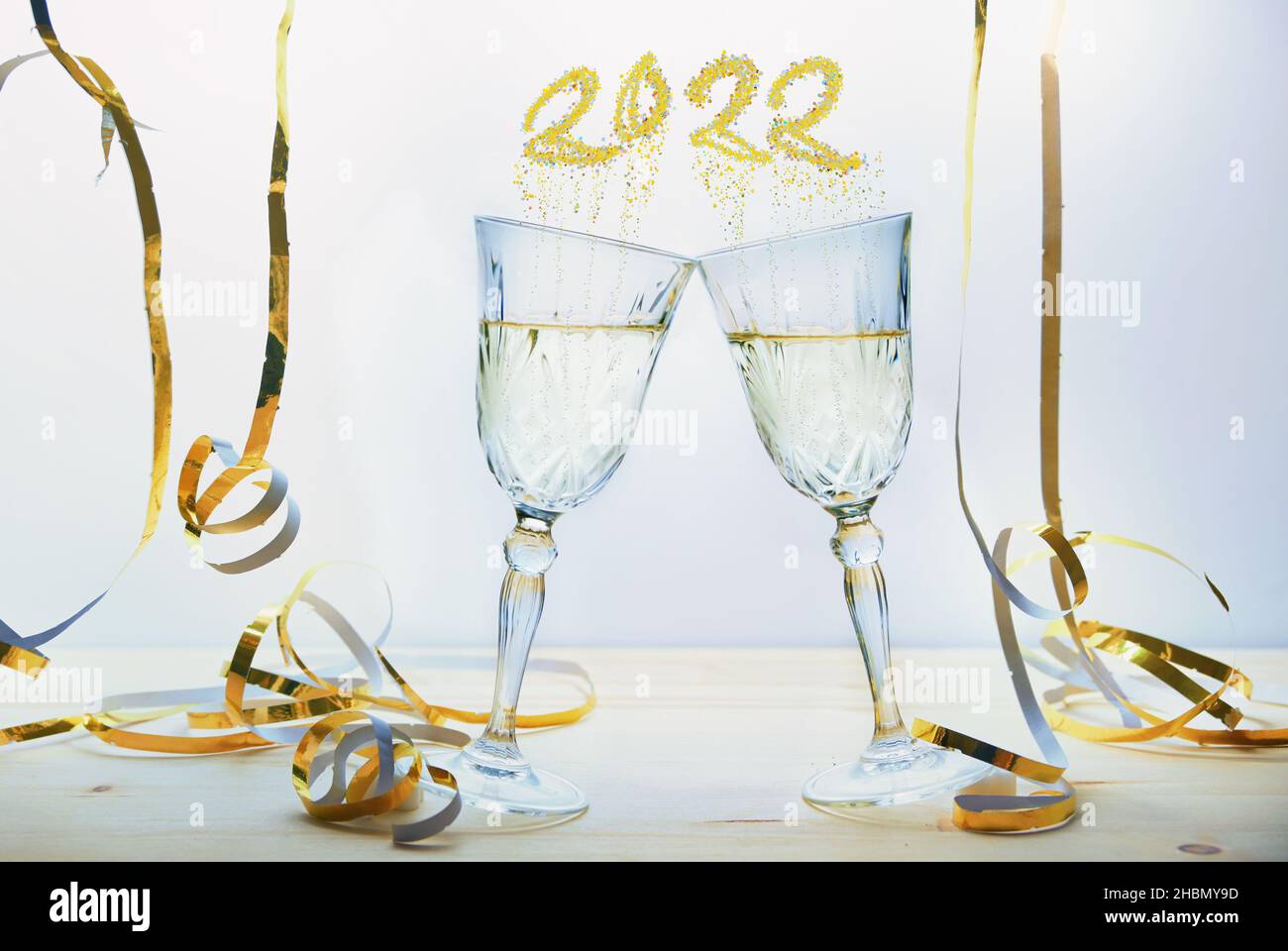 Due bicchieri di champagne brinda a nuovo anno tra le streamers dorate, bolle a forma di numero 2022, sfondo chiaro, fuoco selezionato, stretta profondità di fie Foto Stock