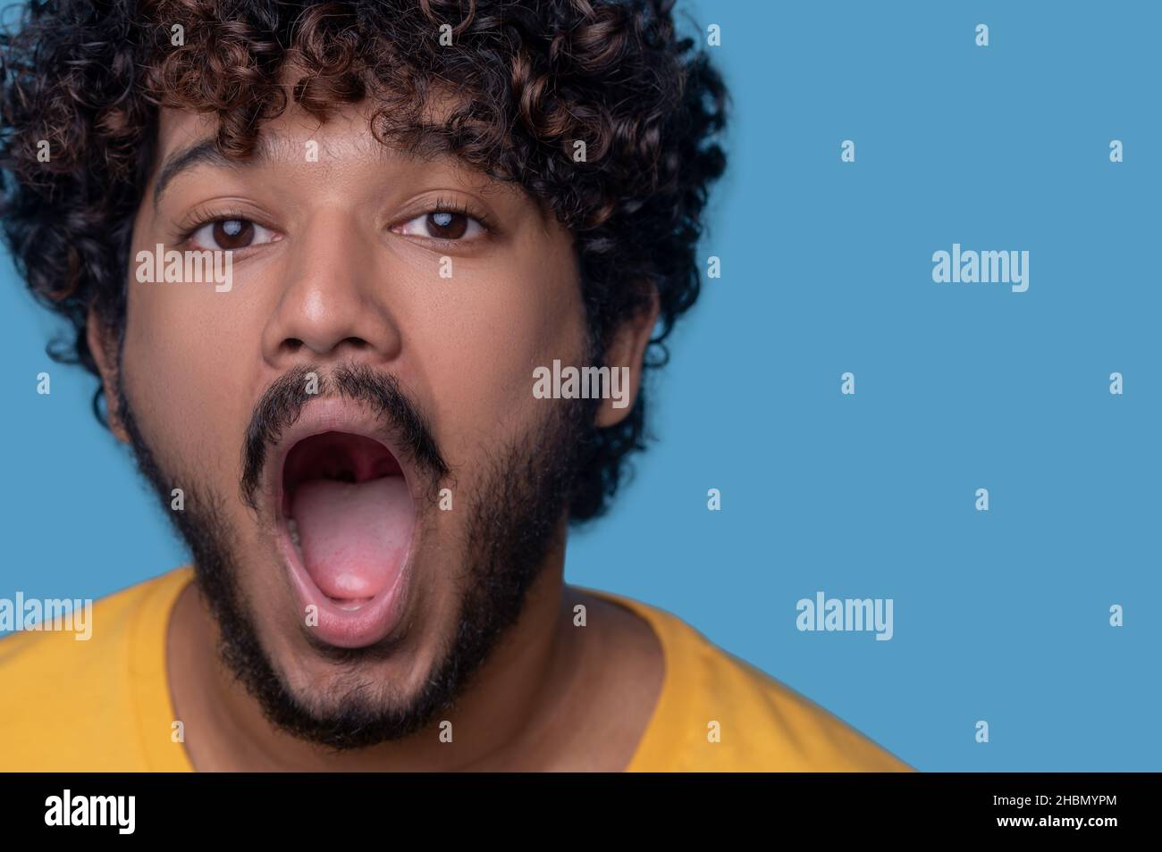 Giovane uomo con bearded capelli ricci a bocca aperta che guarda avanti Foto Stock