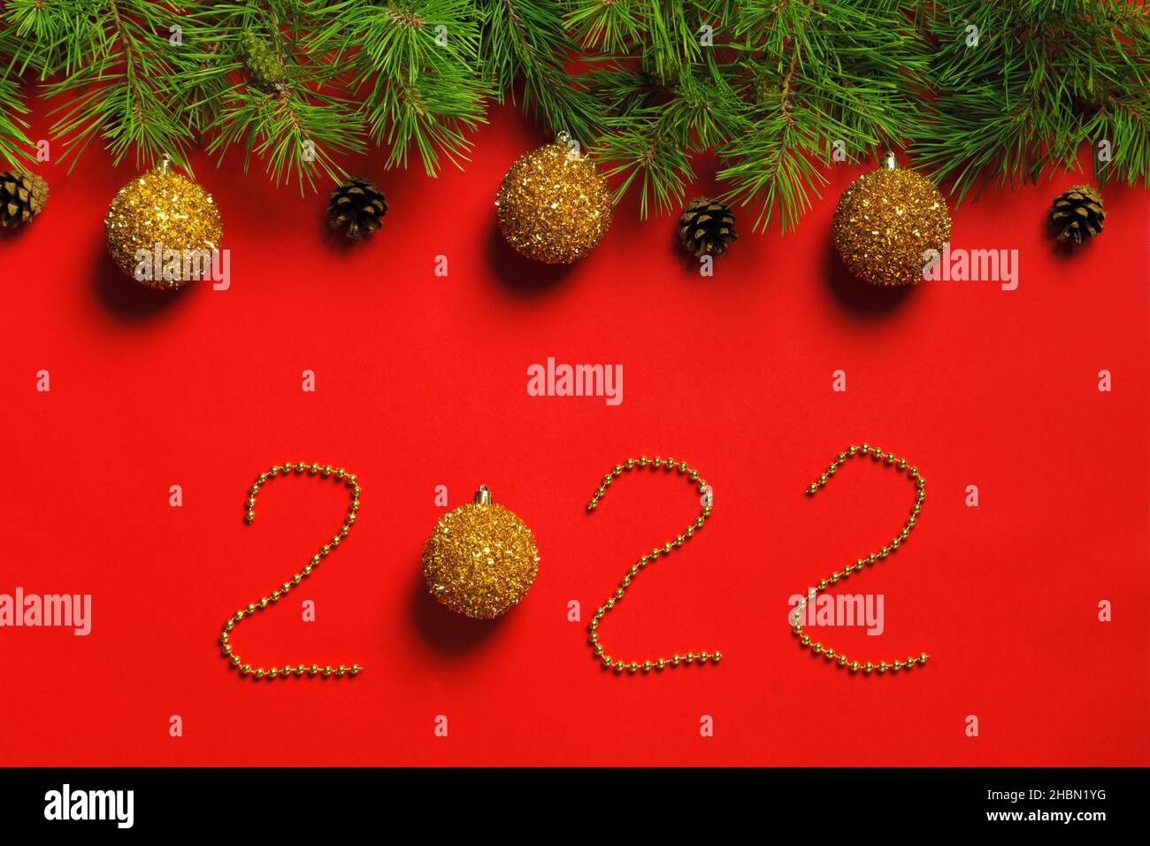 Anno nuovo 2022. Banner natalizio fatto di rami di abete con coni e palline su sfondo rosso. Beads che scritte i numeri. Foto Stock