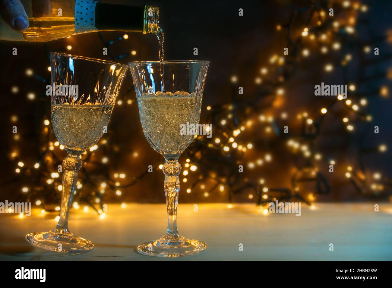 Due bicchieri vengono versati con champagne per un brindisi di Capodanno, luci dorate bokeh su sfondo scuro, spazio copia, fuoco selezionato, profondità stretta Foto Stock