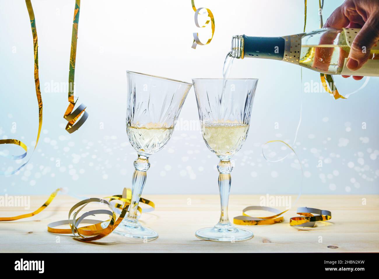 Versando champagne da una bottiglia in due bicchieri per brindare per l'anno nuovo o altre celebrazioni, festive dorate streamers su uno sfondo chiaro, selec Foto Stock