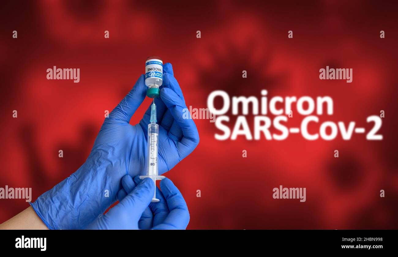 Operatore medico con guanti blu che tengono la siringa e che estrae il vaccino contro il coronavirus dal flaconcino di fronte allo sfondo con testo omicron sars-COV-2 Foto Stock