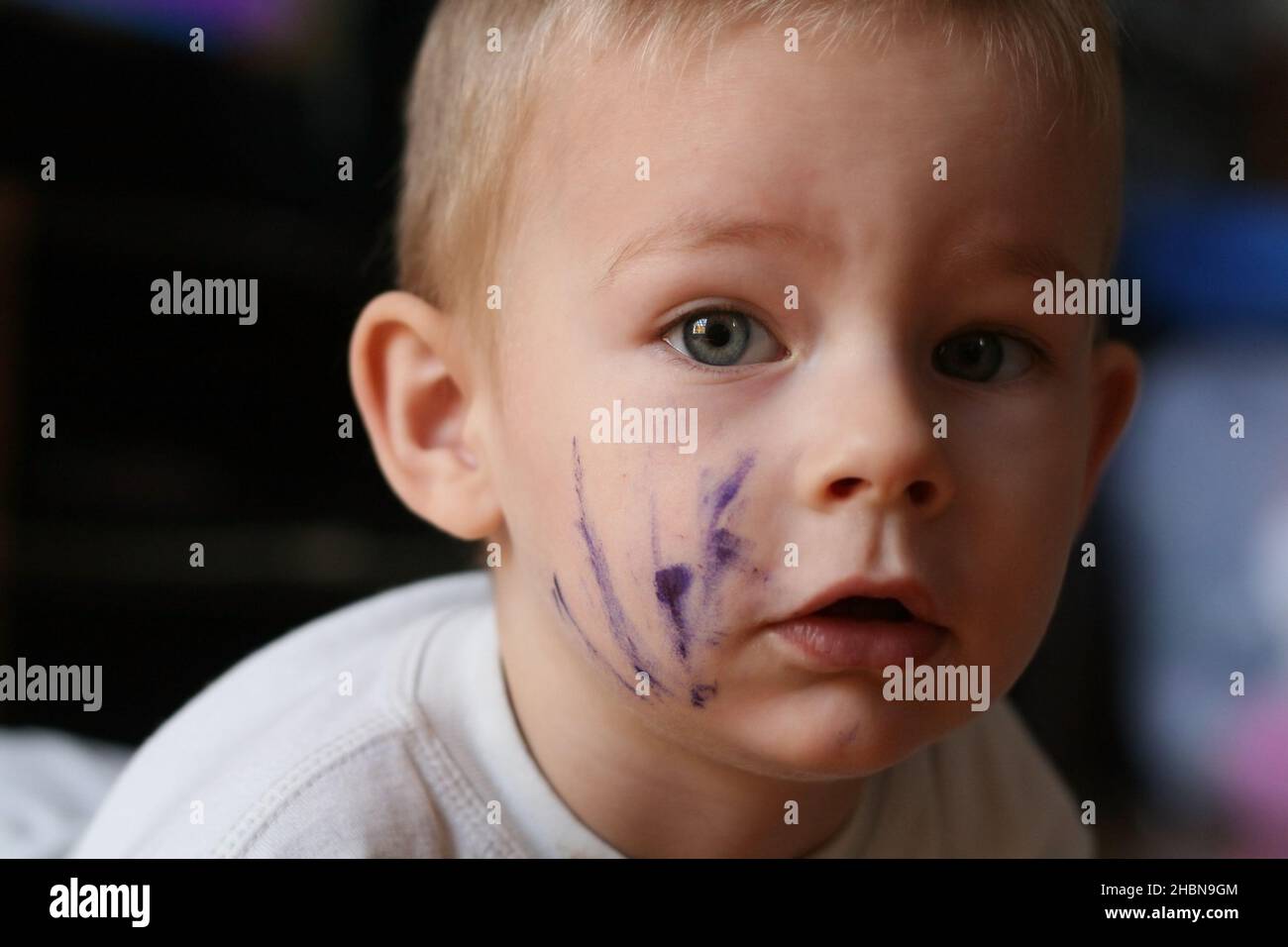 Spensierate il bambino di due anni che ha appena dipinto il suo volto con inchiostro guardando la macchina fotografica Foto Stock