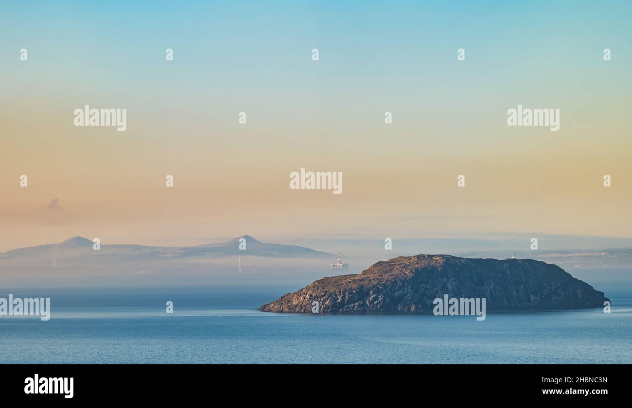 Ammira Firth of Forth con Lamb Island e le cime gemelle delle Lomond Hills viste attraverso la nebbia con una piattaforma di perforazione petrolifera in lontananza, Scozia, Regno Unito Foto Stock