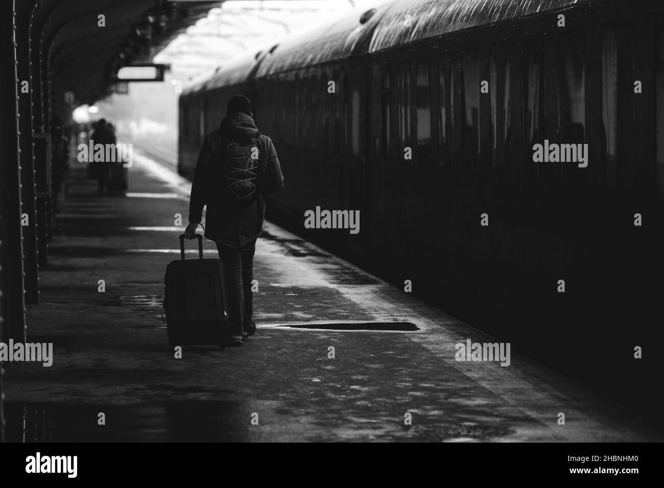 Bianco e nero e (film noir, atmosferica) immagine con un uomo che porta un bagaglio vicino ad un treno pronto a partire da una stazione ferroviaria su una sint nevoso freddo Foto Stock