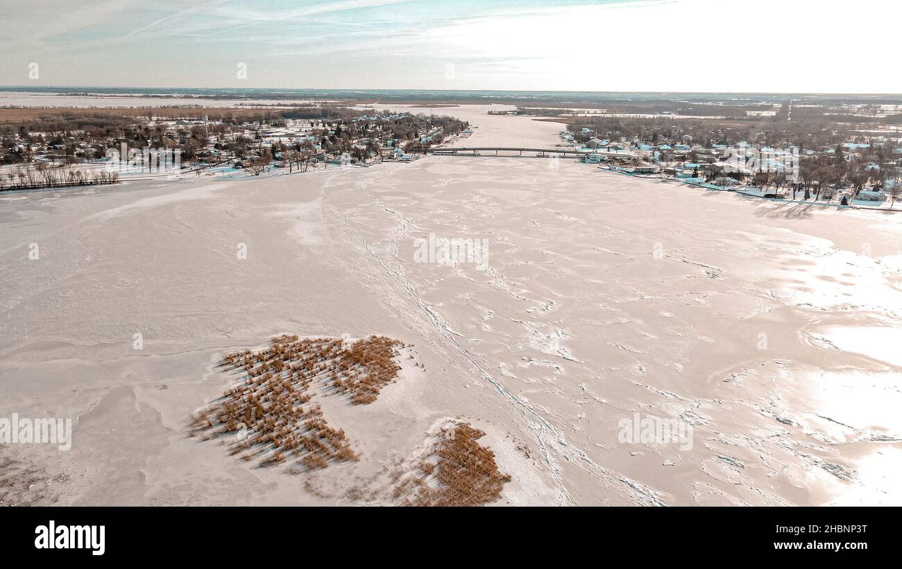 Alto angolo di vista sul lago di Winneconne ghiacciato e la città stessa con ponte. La neve fresca il giorno prima copre il lago con cielo limpido. Foto Stock