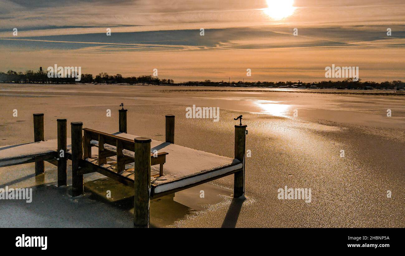 Prendi posto sulla panchina e guarda verso l'esterno fino al sole luminoso che si affaccia sul lago ghiacciato dopo una nevicata fresca. Foto Stock