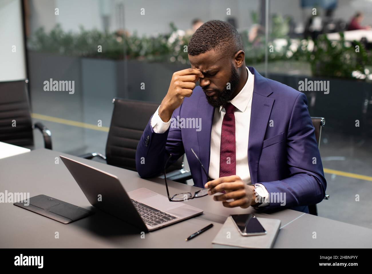 Esausto uomo d'affari afroamericano che lavora su un portatile in ufficio Foto Stock