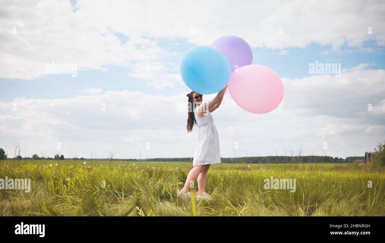 Ragazza felice con grandi palloncini multicolore in posa sul campo. Foto Stock