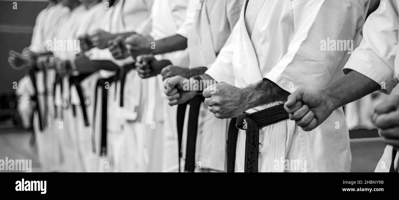 Il maestro di Karate in un kimono bianco e con una cintura nera, si trova di fronte alla formazione dei suoi studenti. Scuola di arti marziali in formazione in palestra. Foto Stock
