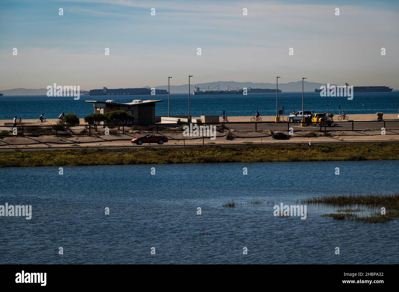 La Bolsa Chica Wetlands, con autostrada, spiaggia, ciclisti e in attesa di navi da carico ancorate al largo in attesa di scaricare nel porto di Long Beach. Foto Stock