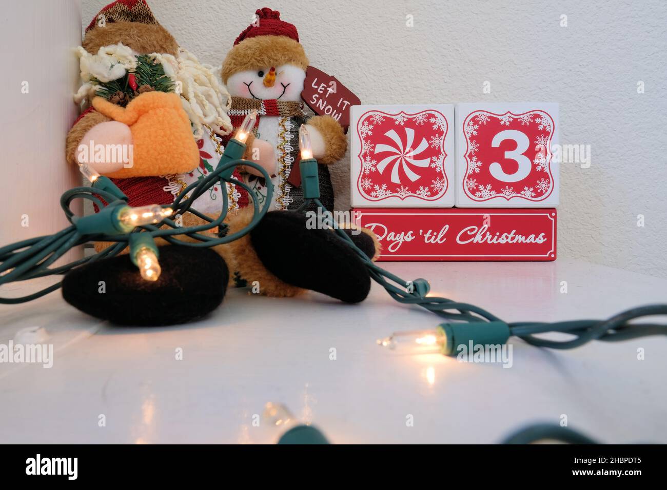 Calendario del conto alla rovescia di tre giorni fino a Natale fatto di blocchi di legno su un mantello con luci e un pupazzo di neve peluche. Foto Stock