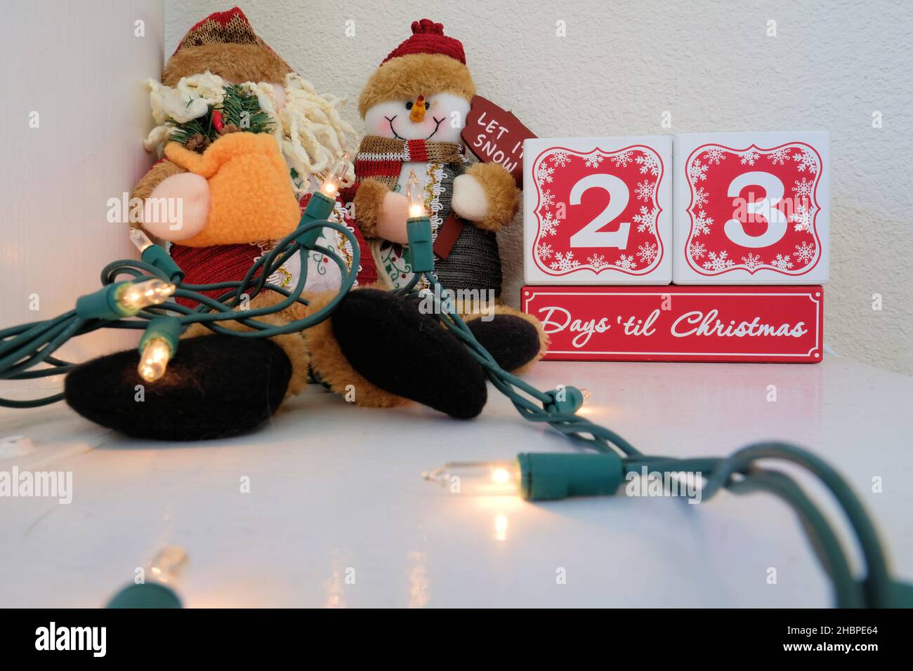 Ventitre giorni 'fino a Natale conto alla rovescia calendario fatto di blocchi di legno su un mantello con luci e un peluche pupazzo pupazzo di neve. Foto Stock