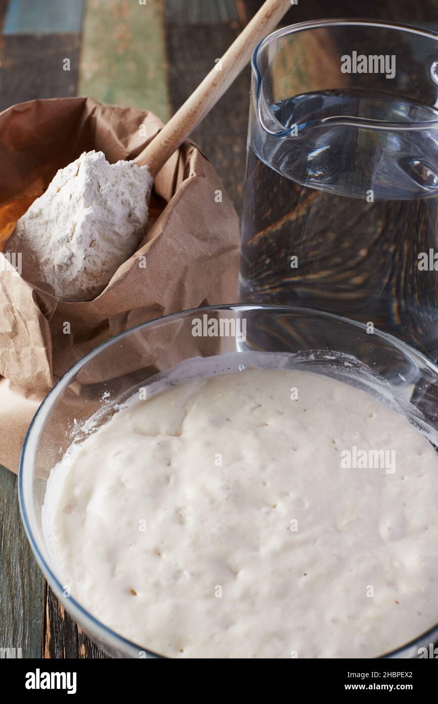 La farina di grano è pronta per essere aggiunta all'impasto. Versare la farina e l'acqua sul tavolo. Vista frontale. Foto Stock