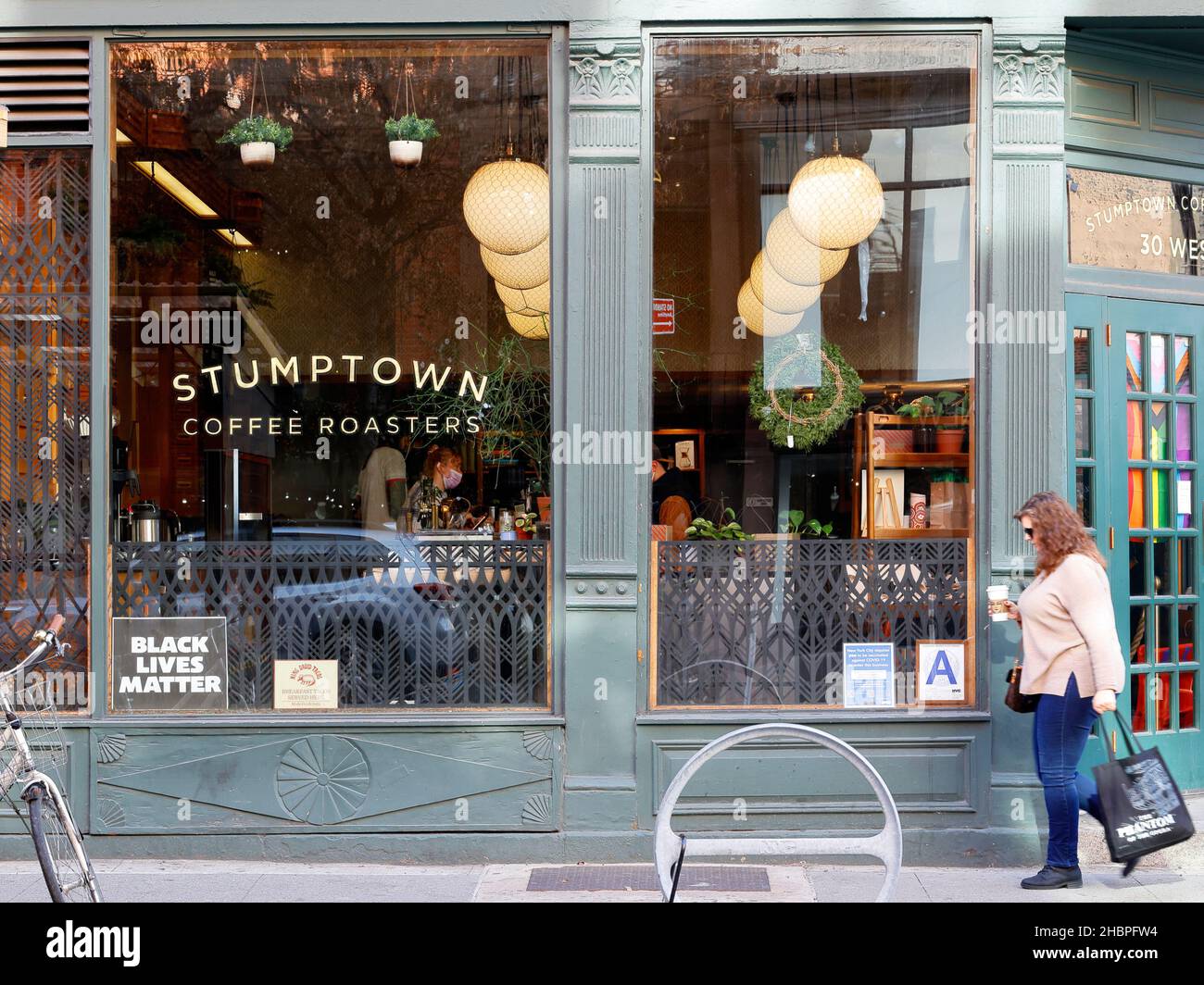 Una donna che tiene una tazza di caffè Starbucks cammina davanti a un'ubicazione Stumptown Coffee Roasters a New York, New York. Foto Stock