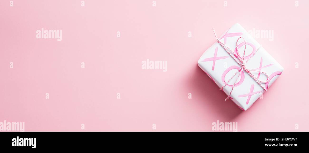 Happy San Valentino banner design con confezione regalo. Confezione regalo in carta bianca con cartello XO su sfondo rosa. Vista dall'alto, spazio di copia. Foto Stock