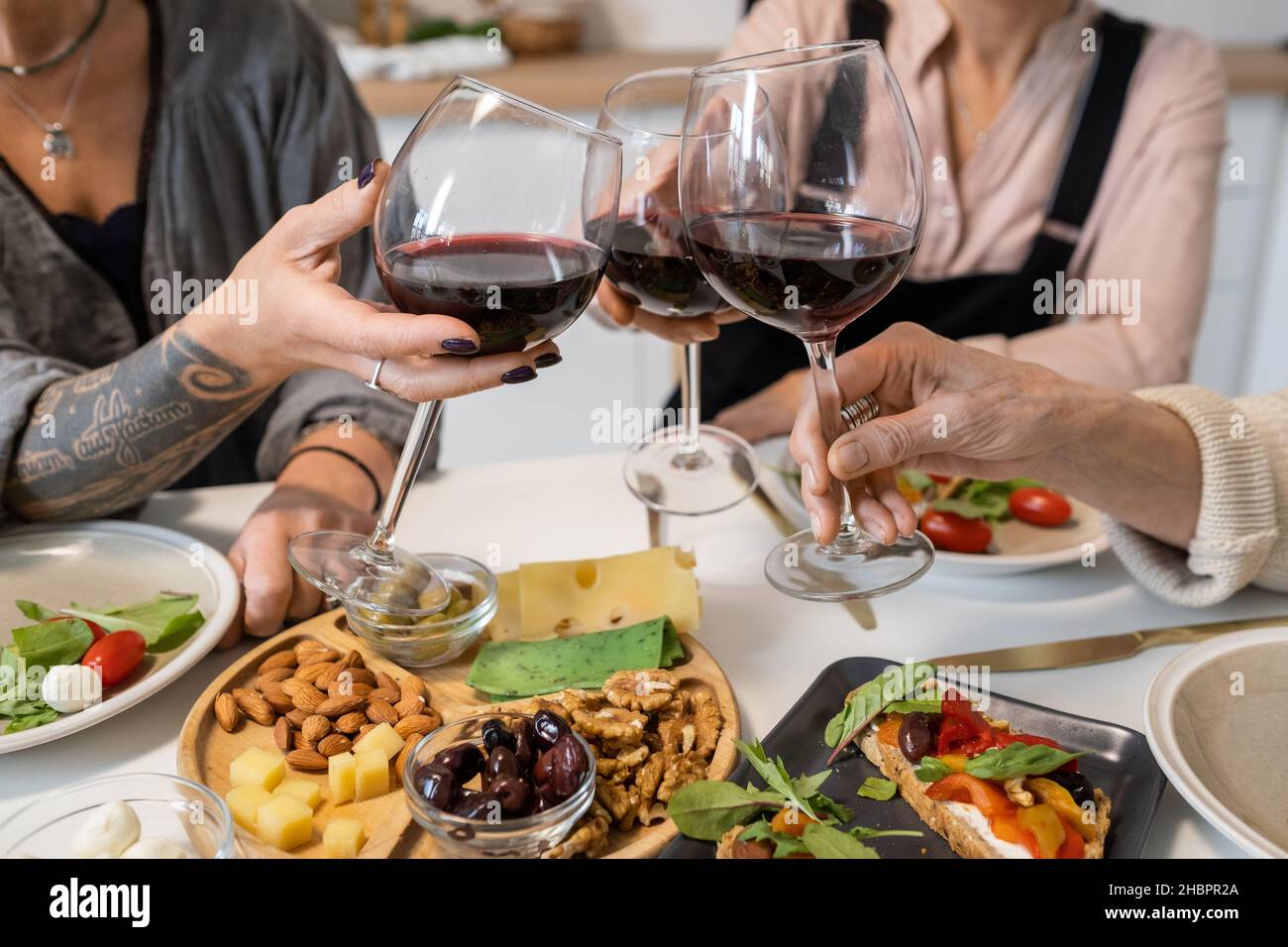 Primo piano di donne che tostano con bicchieri di vino rosso mentre si siede al tavolo da pranzo con antipasti Foto Stock