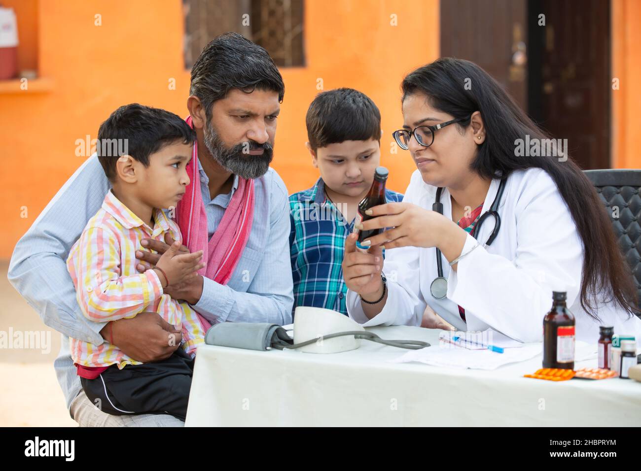Giovane medico indiano femmina con famiglia rurale dare medicina all'aperto villaggio ospedale, Healthcare campo di governo concetto. Padre con i suoi due figli gettin Foto Stock