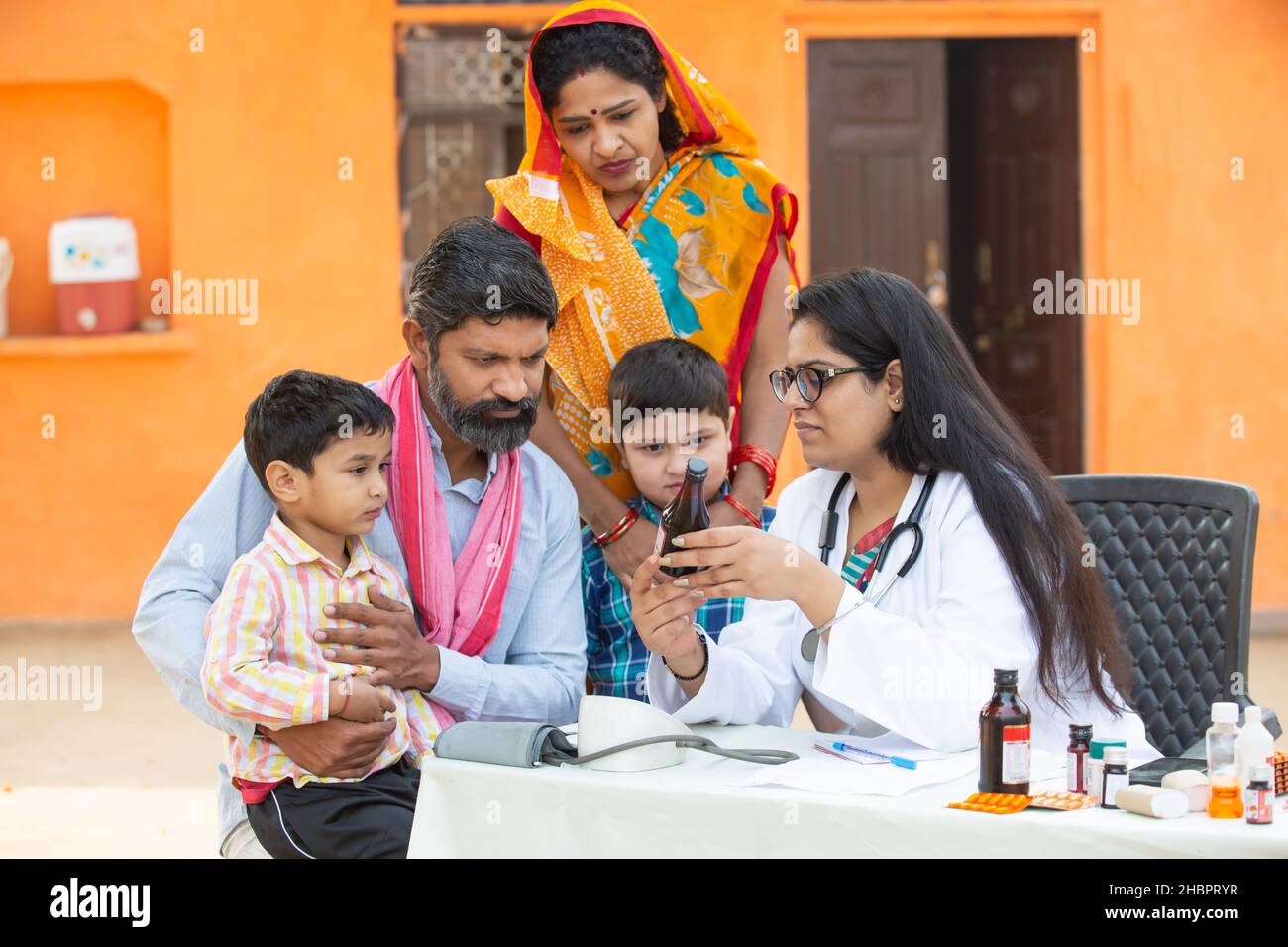 Giovane medico indiano femmina con famiglia rurale dare medicina all'aperto villaggio ospedale, Healthcare campo di governo concetto. Genitori con due figli che ottengono m Foto Stock