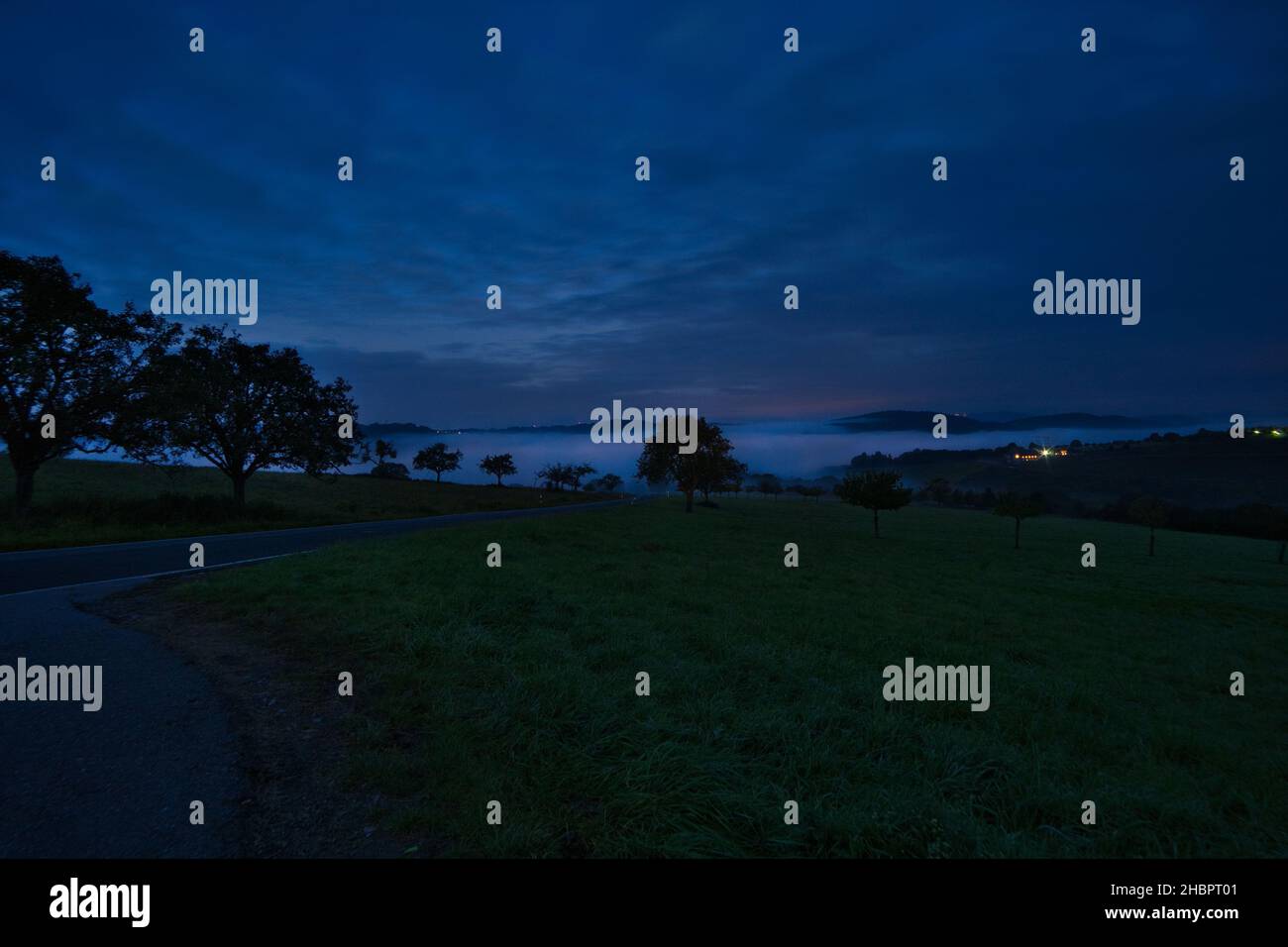 strada con alberi e prati all'ora blu di sera, sullo sfondo piccole montagne, colline nel palatinato. Foto Stock