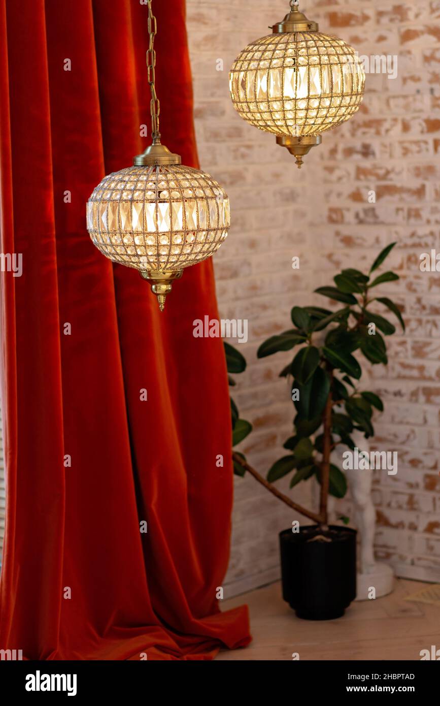 Un moderno interno francese con tende Bordeaux cordurose e lampadari di cristallo contro una parete di mattoni. Messa a fuoco selettiva soft. Foto Stock