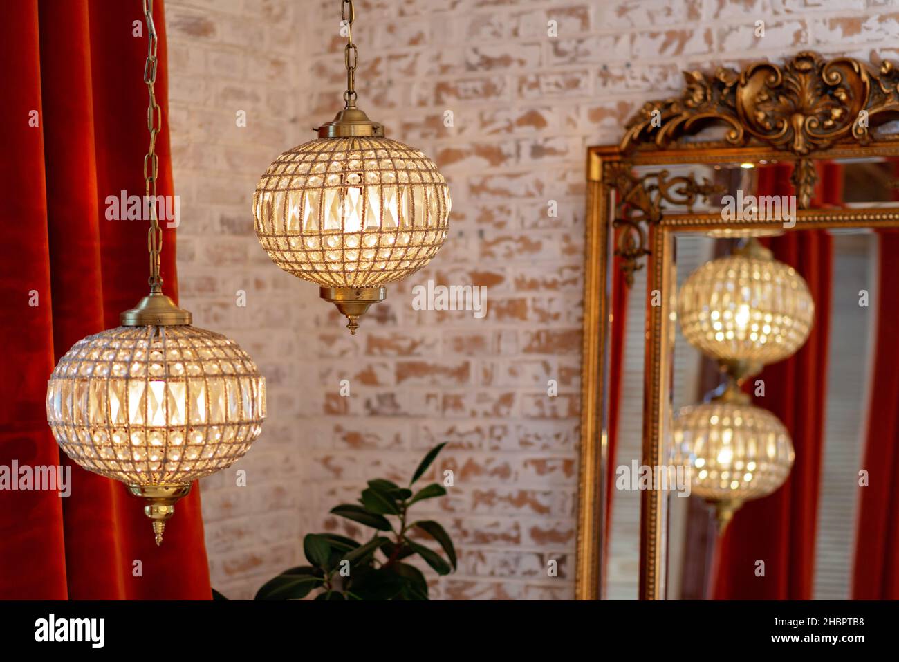Interni francesi moderni con tende bordeaux corduroy, specchio d'oro vintage e lampadari di cristallo contro una parete di mattoni. Messa a fuoco selettiva soft. Foto Stock
