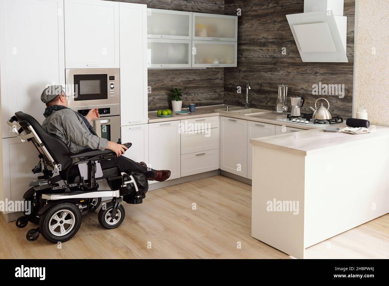 Uomo di mezza età con disabilità seduta da forno elettrico in grande cucina confortevole in ambiente domestico Foto Stock