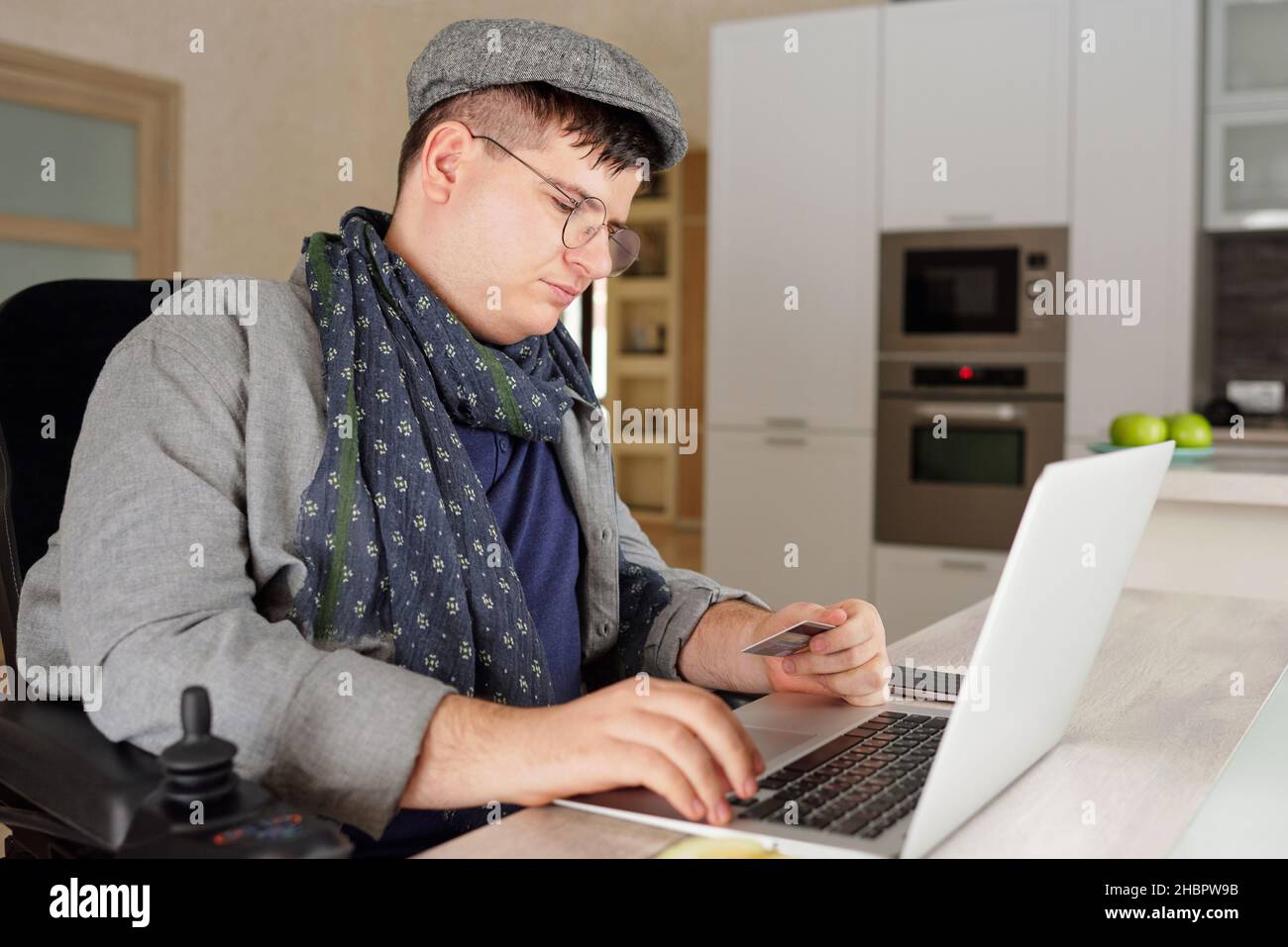 Giovane uomo contemporaneo con disabilità fare ordine nel negozio online mentre si paga per le merci o l'acquisto con carta di credito Foto Stock