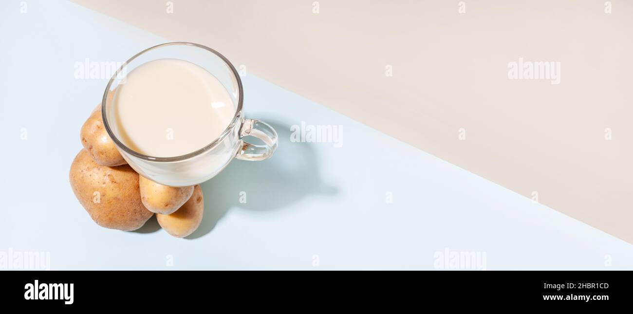 Latte vegetale alternativo. Composizione moderna con una tazza di latte di patate che si bilancia su un mucchio di patate. Foto Stock