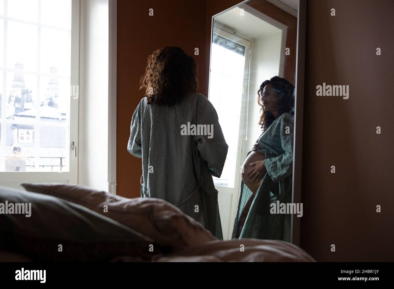 Donna incinta che guarda nello specchio della camera da letto Foto Stock