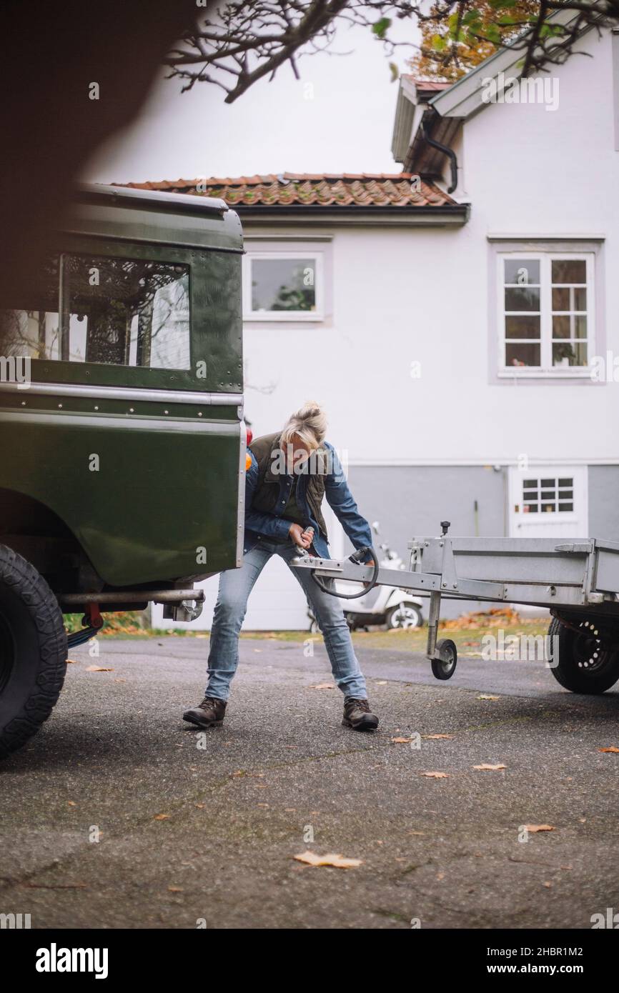 Donna matura che traina un rimorchio su un veicolo di servizio sportivo sul vialetto di guida Foto Stock