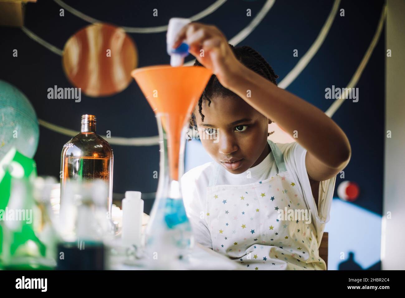 Ambiziosa ragazza che mescola la soluzione chimica mentre imparano il progetto scientifico al tavolo Foto Stock