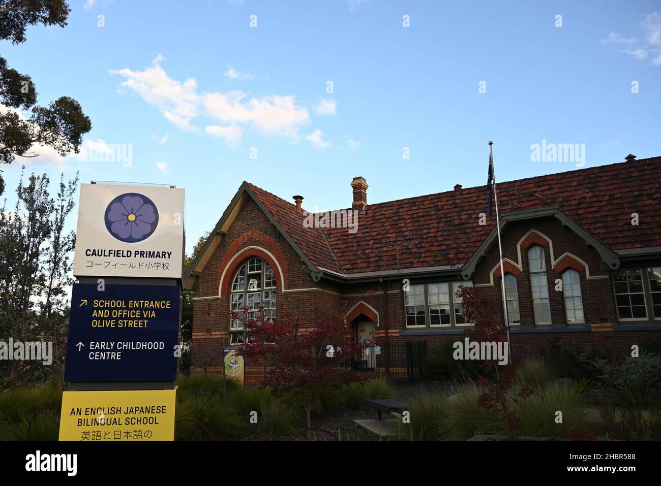 Segnaletica bilingue inglese e giapponese all'ingresso della scuola elementare di Caulfield su Glenhuntly Road, con un edificio scolastico e giardino sullo sfondo Foto Stock
