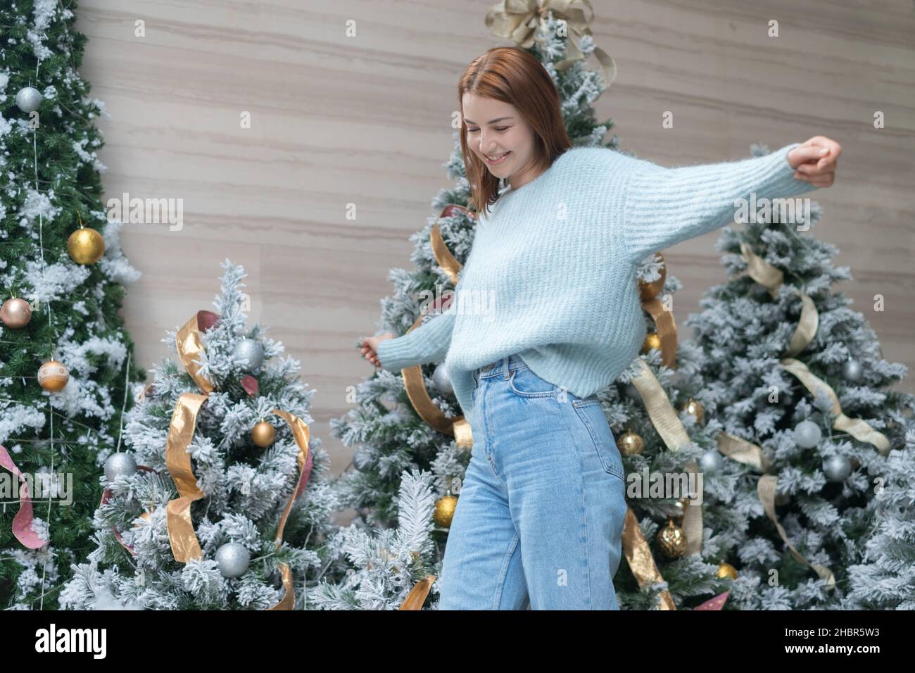 Ritratto di Capodanno di bella ragazza caucasica sorridente in lana accogliente caldo azzurro maglione in piedi vicino decorato albero di Natale. Persona felice Foto Stock