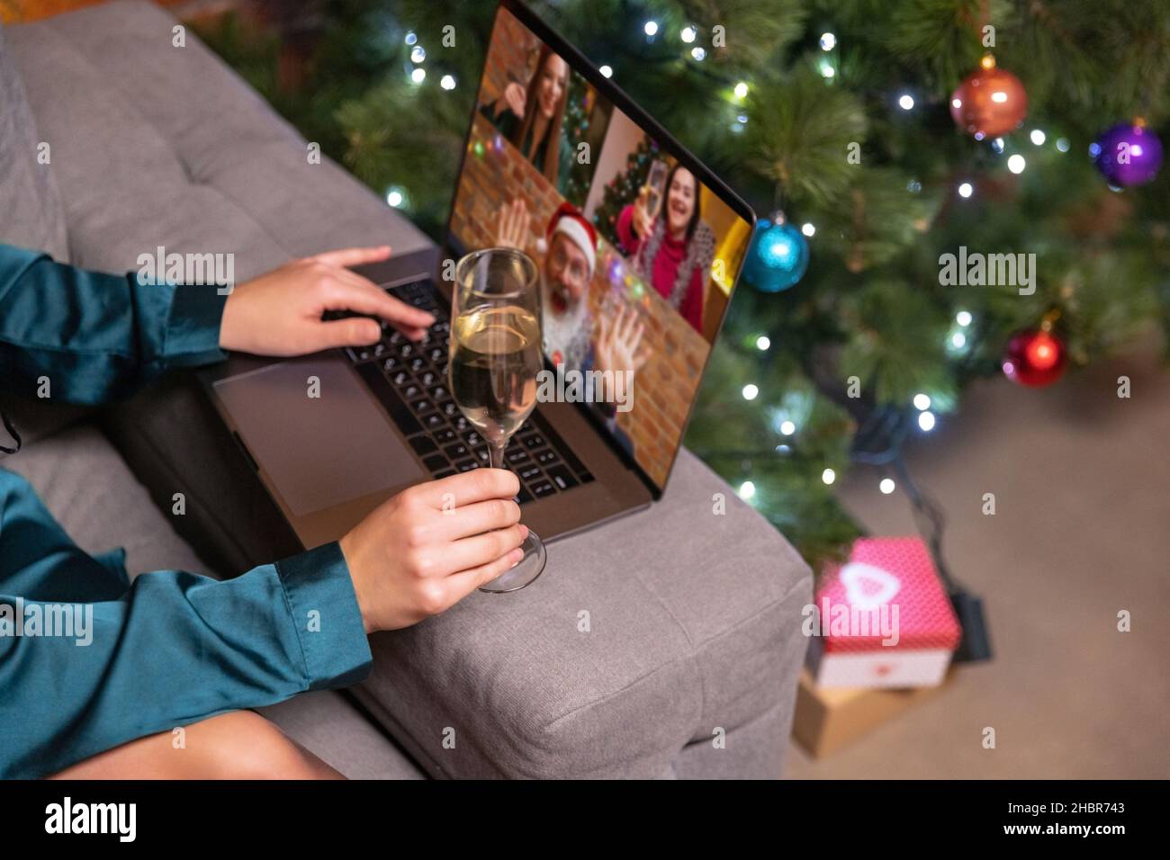 Primo piano mani femminili con bicchiere di champagne, utilizzando il computer portatile e parlando con amici, famiglia tramite videochiamata. Foto Stock