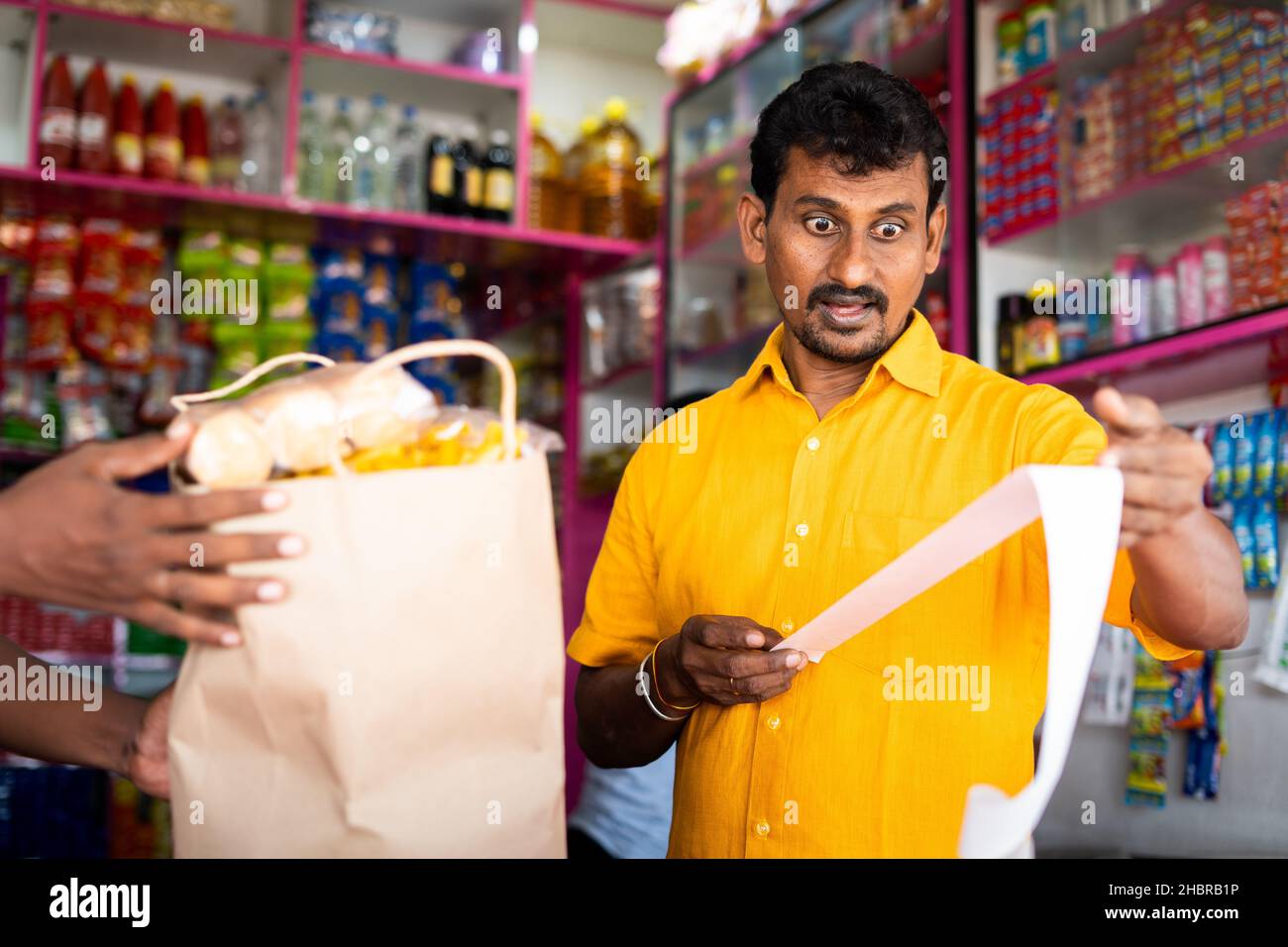 Cliente scioccato a Kirana o negozio di alimentari dopo aver visto la ricezione di fatture alimentari - concetto di inflazione, aumento dei prezzi e consumismo. Foto Stock