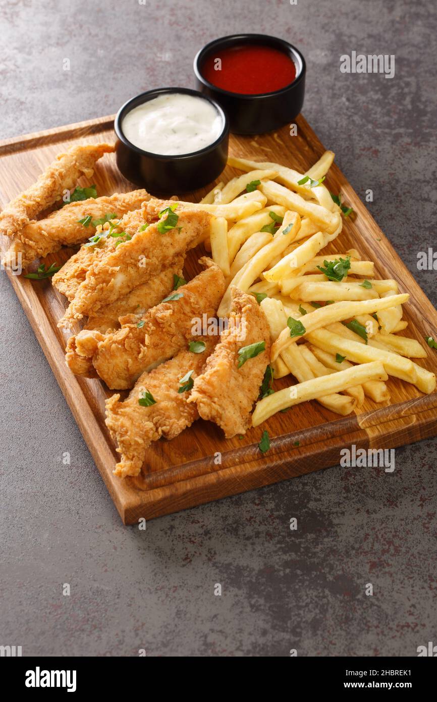 Strisce di pollo croccanti fatte in casa e patate fritte primo piano sul vassoio di legno su un tavolo di cemento. Verticale Foto Stock