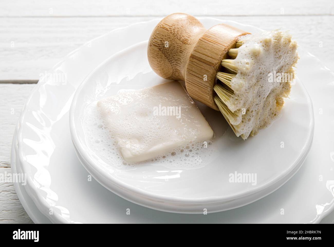 Sapone per piatti solido, ricoperto di schiuma. Stile di vita senza sprechi. Sapone per lavastoviglie su pelo di piatti con spazzola in sisal per la pulizia della cucina schiumosa. Foto Stock