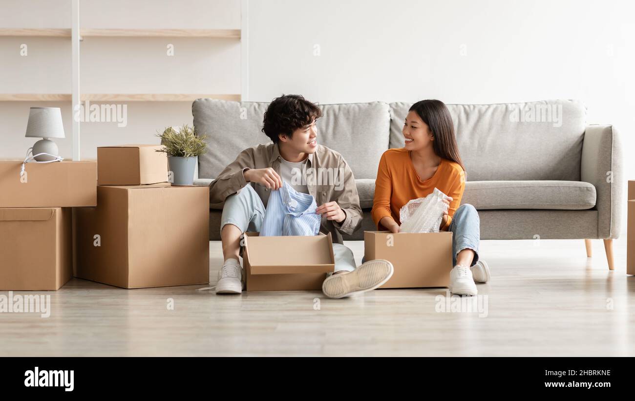 Allegro coppia asiatica disimballaggio effetti personali e di avere conversazione, il trasferimento in un nuovo appartamento o la loro casa Foto Stock