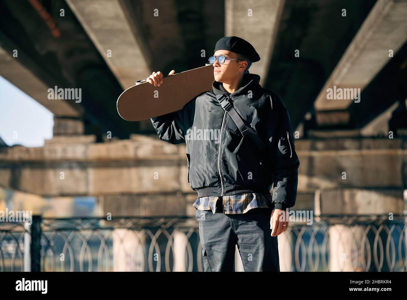 Skater maschio con skateboard in posa su sfondo urbano strada. Concetto di sport estremi Foto Stock