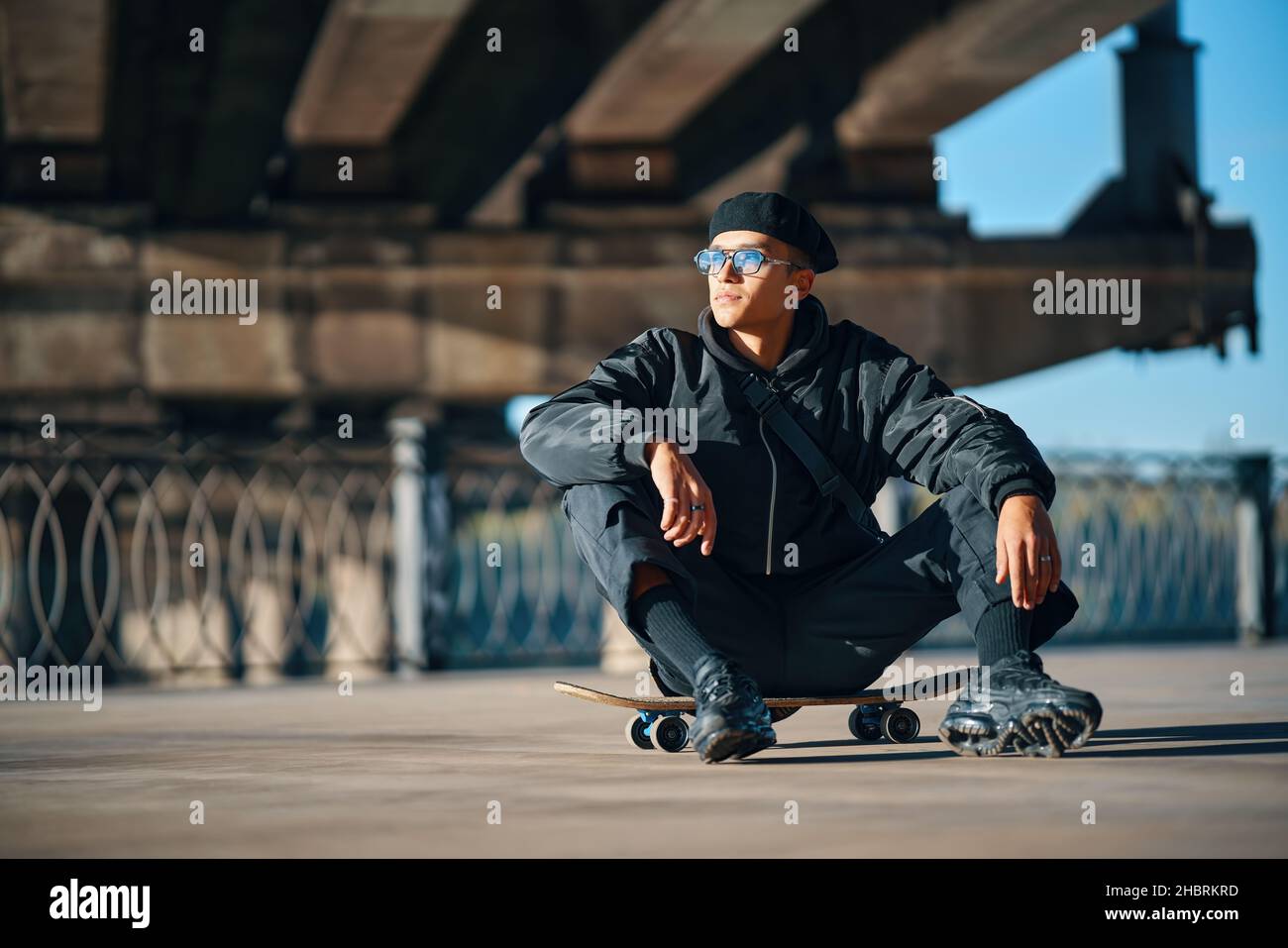Skater maschio relax seduta su skateboard su sfondo urbano strada. Concetto di sport estremi Foto Stock