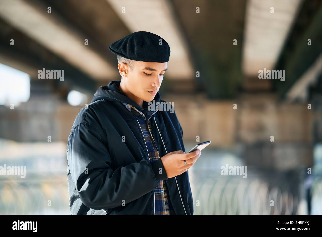 Uomo di hipster millenario che usa lo smartphone su sfondo urbano della strada Foto Stock