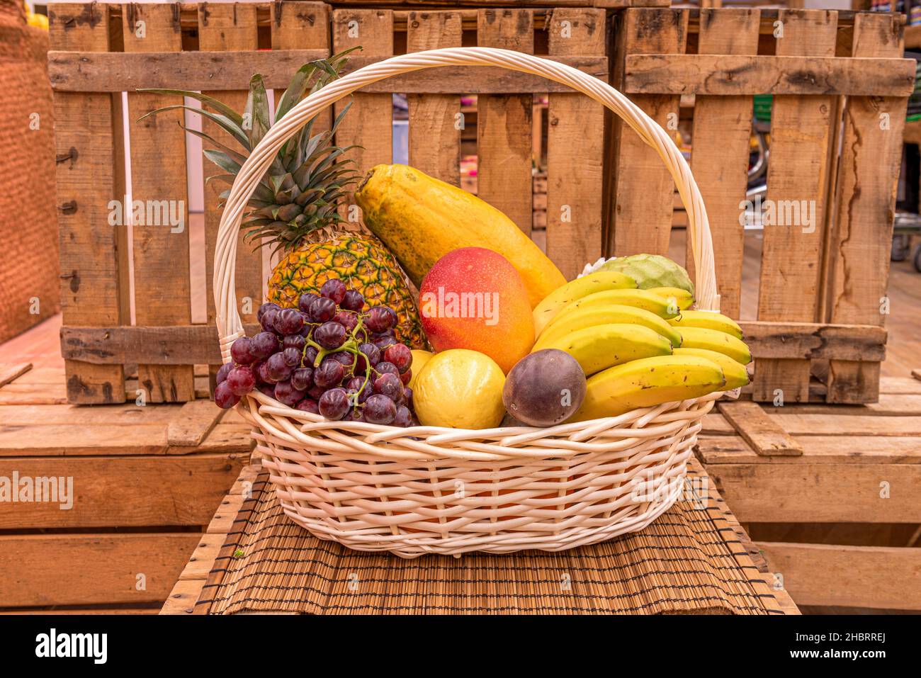 Cestino di vimini non verniciato pieno di frutta fresca, banane, mango, prugne e ananas Foto Stock