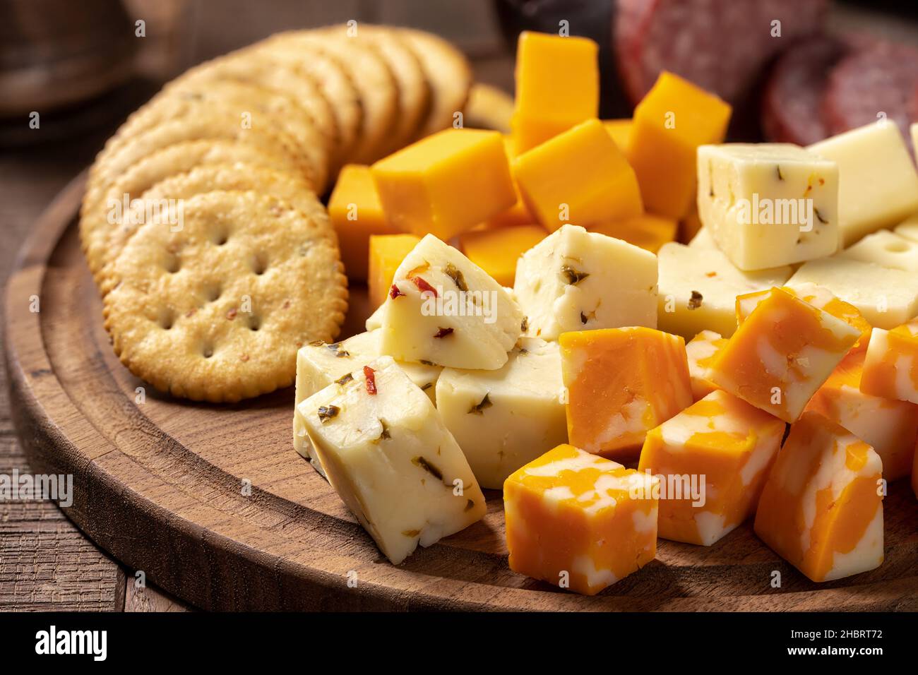 Assortimento di cubetti di formaggio con cracker e salsiccia su un piatto di legno Foto Stock