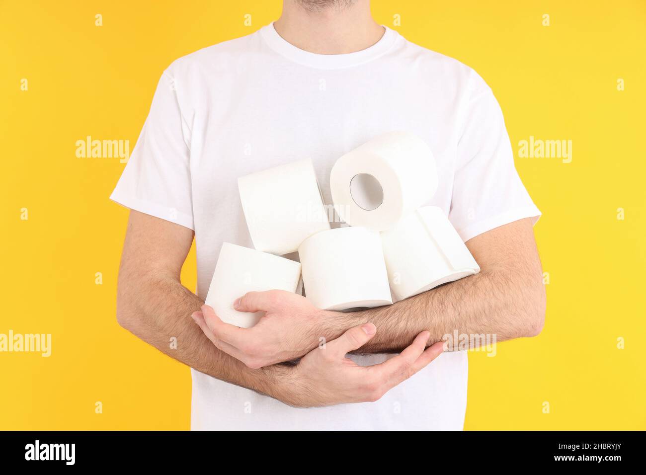 L'uomo tiene la carta igienica su sfondo giallo. Concetto di Emorroidi Foto Stock