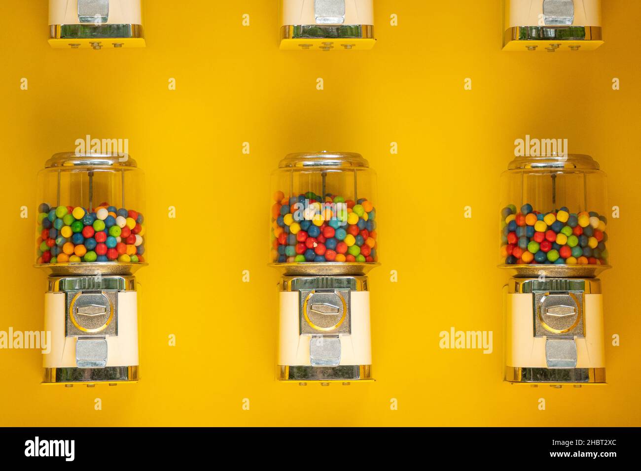 Distributori automatici di gumball contro un muro giallo Foto Stock