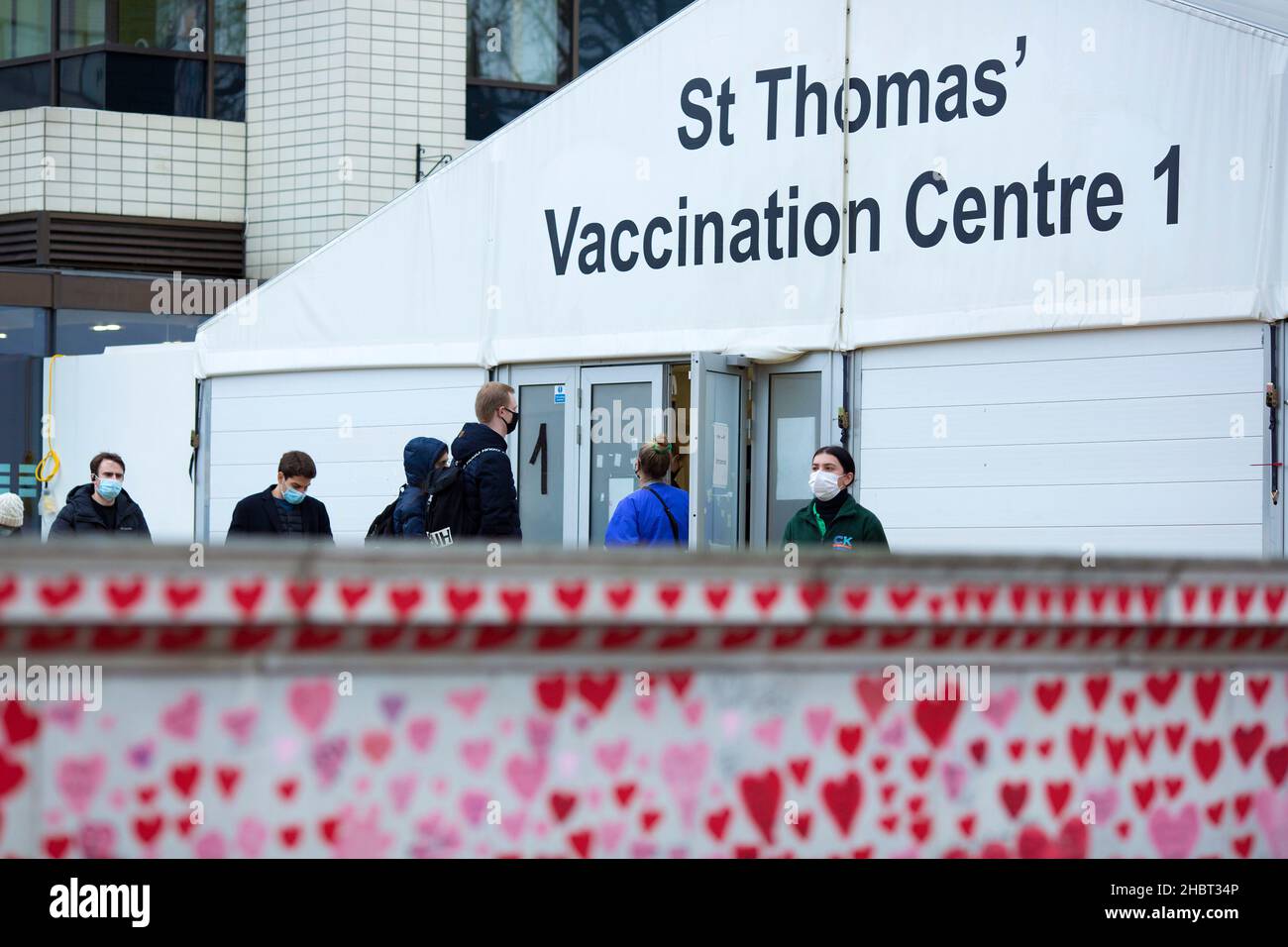 Le persone sono viste fare la fila verso un centro di vaccinazione al St Thomas’ Hospital dietro i cuori rossi dipinti sul National Covid Memorial Wall di Londra. Foto Stock