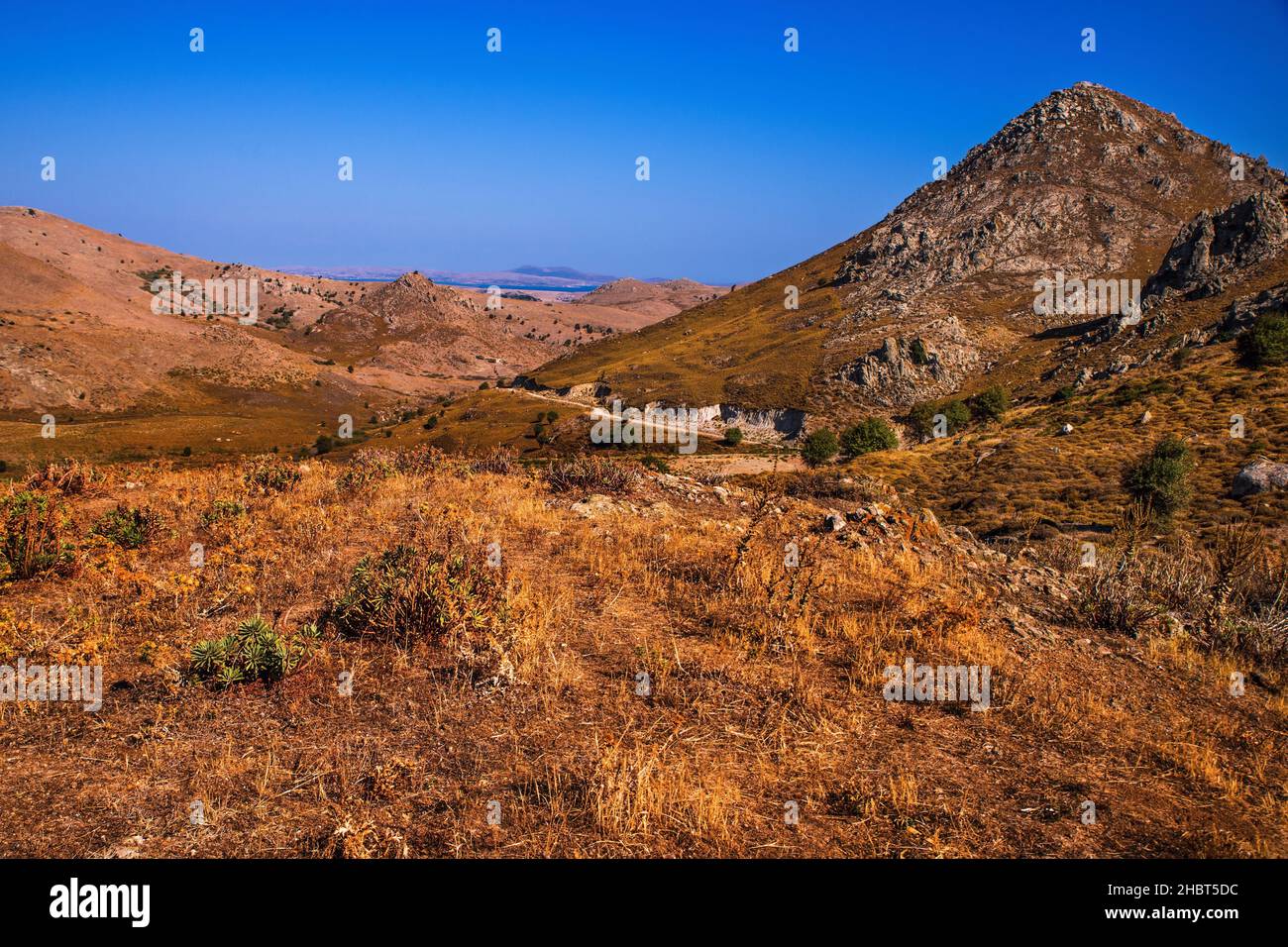 Paesaggio roccioso, vulcanico interno con collina a spiked, vegetazione secca di timo a fine estate, mare sullo sfondo, bellezza selvaggia dell'isola di Linnos, Grecia. Foto Stock