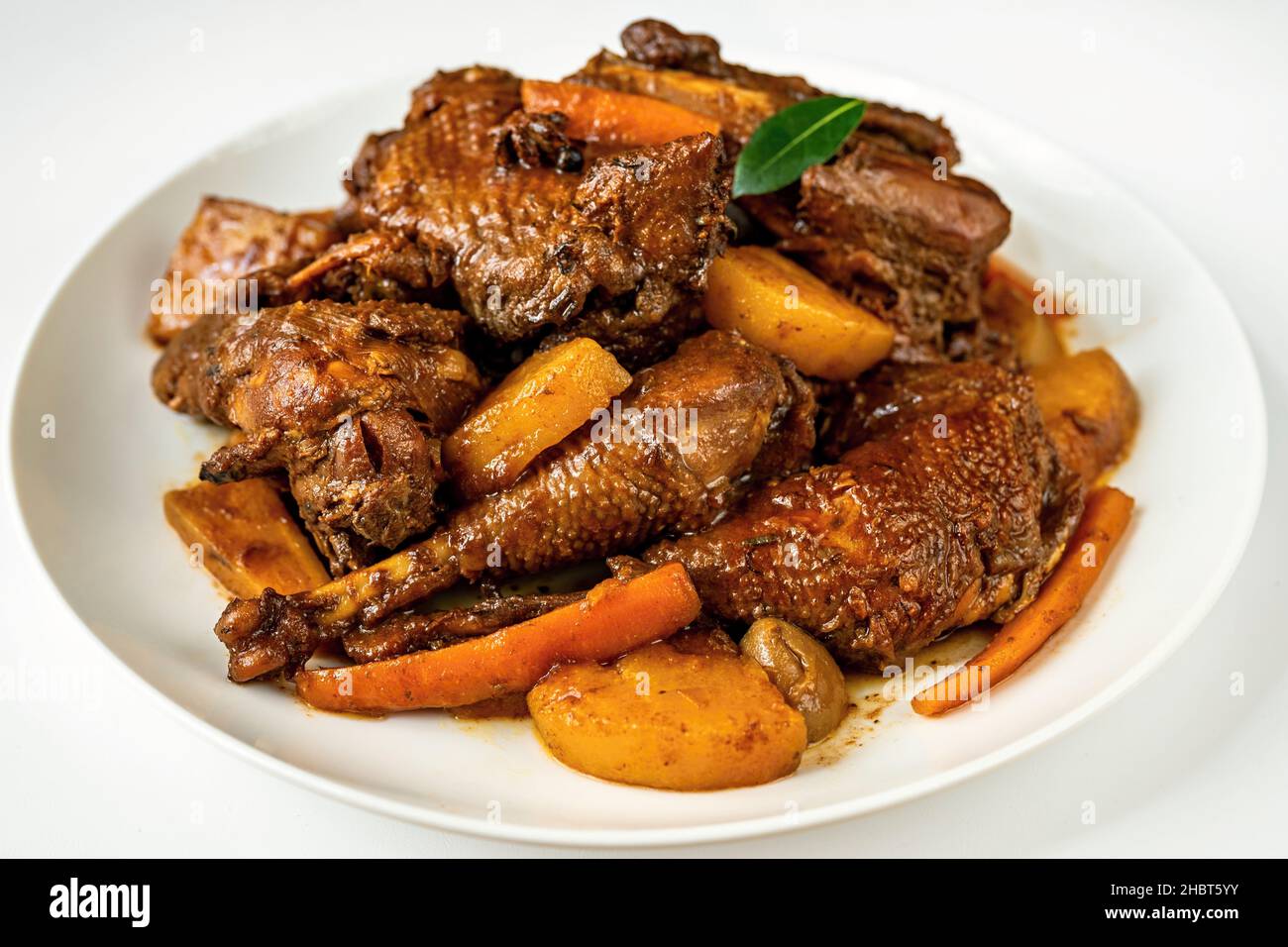 Piatto bianco con molti pezzi di gallina al forno con carota, pera e spezie. Specialità della vecchia Boemia. Sfondo bianco, primo piano. Foto Stock